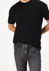 Černé bavlněné tričko s ohrnutými rukávy v kombinaci s tmavě šedými džíny, které mají klasický pětikapsový design a viditelné švy.