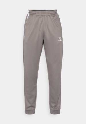 Grijze sportbroek met een elastische tailleband, taps toelopende benen en witte accenten aan de zijkant. Bevat een klein merkje op de bovenbeen. Glad textuur.