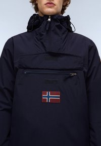 Marineblå genserjakke med høy krage, justerbar hette, en glidelåslomme og et Norge-flag patch på forsiden.