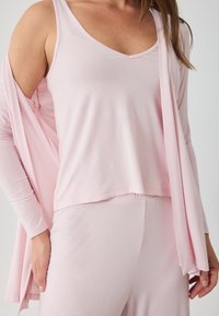 Σειρά ρούχων σε απαλό ροζ απόχρωση, που περιλαμβάνει ένα αμάνικο τοπ με V-λαιμόκοψη και μια μακριά, ανοιχτή κάρντιγκαν. Απαλή, ομαλή ύφανση με χαλαρή εφαρμογή.