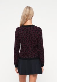 Maroon sweater featuring a black leopard print, round neck, and black ribbed cuffs and hem. Worn with a black pleated skirt.
