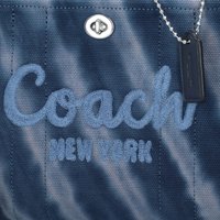 Navy fabric tote with embossed light blue "Coach New York" text, silver hardware, and black tag attached by a chain. Textured material.