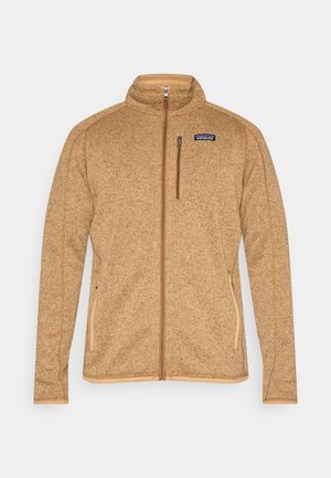 Giacca in pile color cammello con collo alto, cerniera frontale completa, tasche laterali e cuciture a contrasto color cammello lungo le cuciture e i bordi.