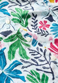 Chemise à boutons avec un tissu léger, présentant un motif floral coloré en vert, bleu, rose et marine sur fond blanc.