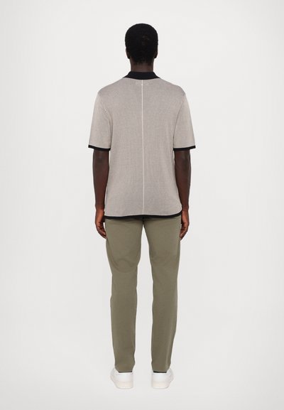 T-shirt noir et beige à manches courtes avec un col rond, associé à un pantalon vert olive clair et des baskets blanches.