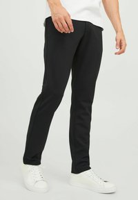Pantalones negros ajustados hechos de un material elástico, con una textura suave y un diseño minimalista, combinados con zapatillas blancas.