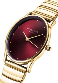 Montre ronde avec un cadran dégradé bordeaux, des index horaires en or et un boîtier en or. Elle est dotée d'un bracelet en métal doré avec une texture polie.