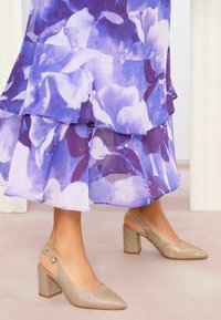 Beige glitteri slingback-kengät, joissa on terävä kärki ja paksu korko, yhdistettynä virtaavaan, kerrokselliseen purppuranväriseen kukkapukuun. Pehmeä, läpikuultava kangas.