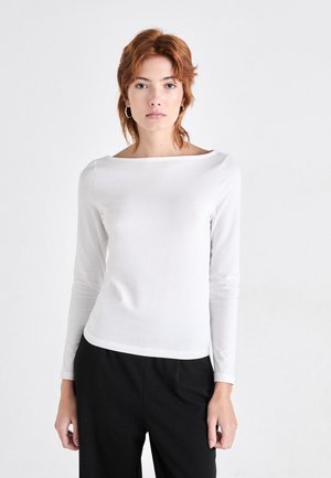 White long-sleeve top with a boat neckline, smooth texture, slim fit, and a straight hem. Paired with black pants.