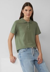 Zielona koszulka polo z kołnierzykiem, krótkimi rękawami i listwą guzikową, połączona z jasnoniebieskimi dżinsami z troczkiem w pasie.