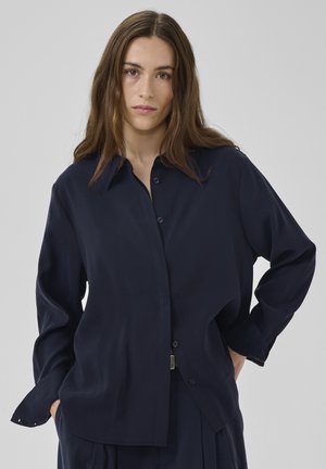 Marineblaues langärmeliges Hemd aus glattem Stoff, ausgestattet mit einem klassischen Kragen, Knopfverschluss und lässiger Passform mit dezenten Manschettendetails.