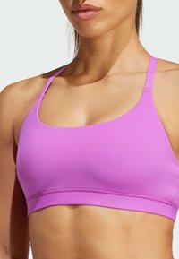 Sujetador deportivo rosa con tirantes finos, textura suave y una banda ancha en la parte inferior. Diseño sencillo, sin herrajes ni patrones visibles.