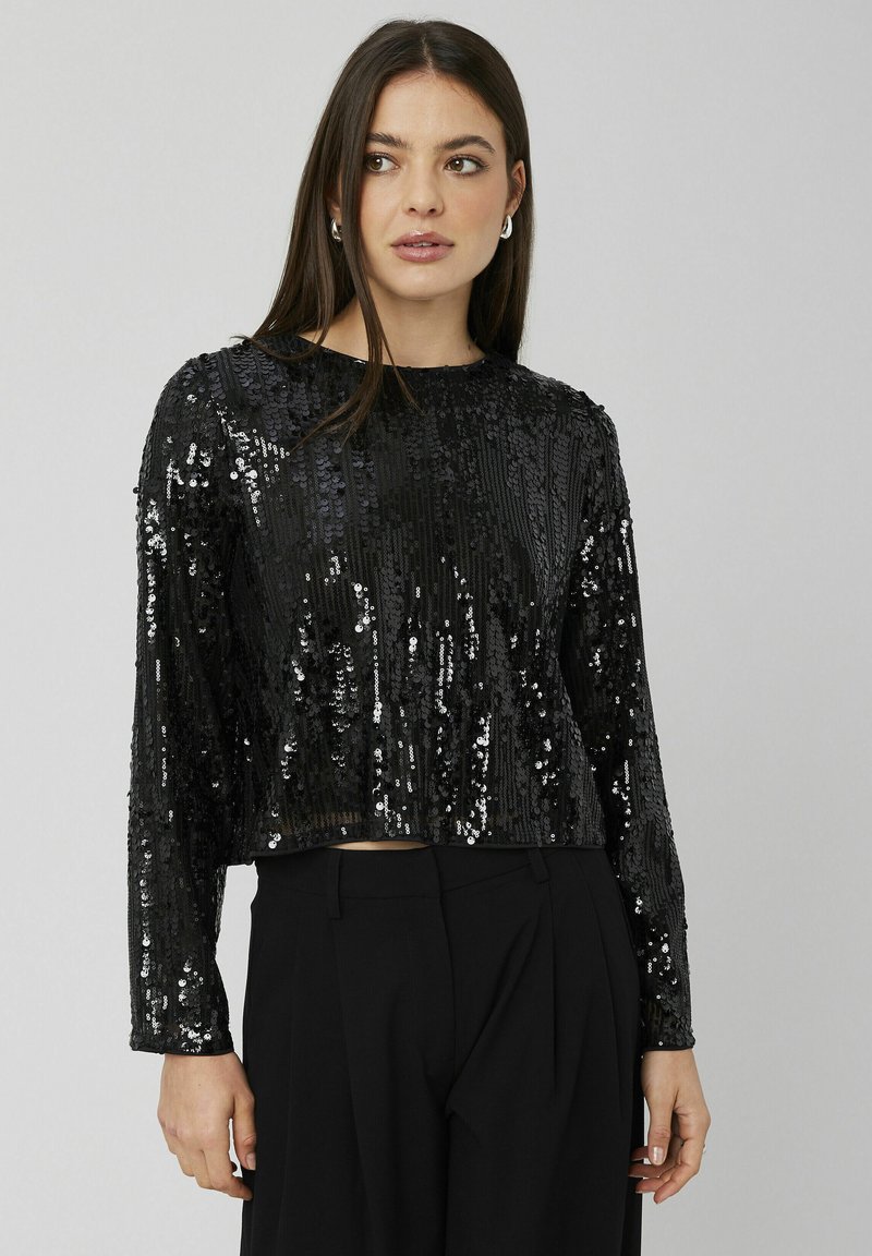 Haut noir à manches longues raccourci en tissu pailleté, avec un design à rayures texturées et un col rond. Porté avec un pantalon taille haute.