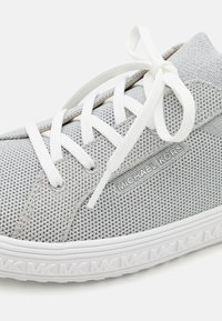 Sneaker grigio realizzato in materiale mesh con lacci bianchi e un accent silver con marchio. Presenta una suola leggera e testurizzata per una migliore aderenza.