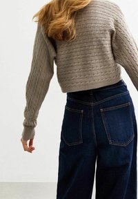 Hellgrauer, kabelgestrickter, gekürzter Pullover mit langen Ärmeln, kombiniert mit hoch taillierten, dunkelblauen Jeans aus Denim, die zwei Gesäßtaschen haben.