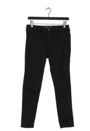 Černé slim-fit džíny zavěšené na černém ramínku s klipsy na bílém pozadí.