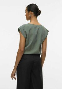 Top verde texturizzato con maniche corte, abbinato a pantaloni neri a gamba larga. Tessuto leggero, design semplice e vestibilità comoda.