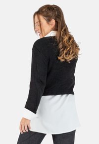 Schwarzer, kurzer Pullover aus strukturiertem Strick, getragen über einem weißen Hemd mit Knöpfen. Mit langen Ärmeln und geripptem Saum.