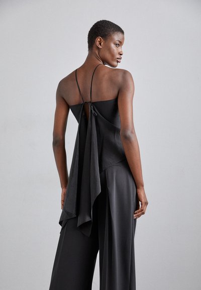 Black sleeveless top with a tie closure at the back, featuring a flowing drape and soft, lightweight fabric. Smooth texture and minimalist design.