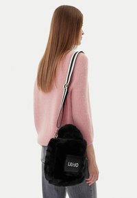 Borsa nera in pelliccia sintetica a forma rettangolare, caratterizzata da una superficie testurizzata, un patch con logo e una tracolla bicolore.