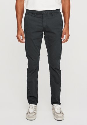 Black trousers made of cotton with a slim fit, featuring a button and zip closure. Worn with light gray sneakers.