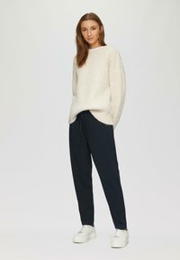 Pull crème surdimensionné à côtes, pantalon noir avec cordon de serrage et baskets blanches à semelle épaisse. Texture douce avec une coupe décontractée et des fentes sur les côtés du pull.