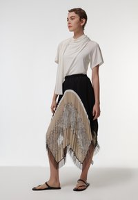Witte korte mouwen top gecombineerd met een zwarte geplooide rok met beige en zwarte kantpatronen, afgewerkt met witte bies en zwarte sandalen.