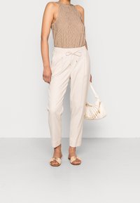 Beżowe lekkie spodnie z regulowanym paskiem w talii, w połączeniu z brązowym, w paski bezrękawnikiem oraz jasnobeżowymi płaskimi sandałami. Biała torebka z łańcuszkiem.