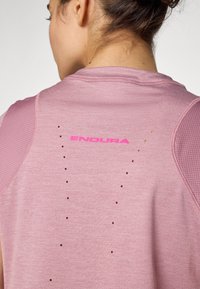 Rožinė sportinė marškinė su tekstūruotu audiniu, tinkliniais akcentais ant pečių ir ventiliacijos angomis. „ENDURA“ logotipas ryškiai rožinės spalvos ant nugaros.