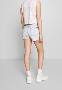 Lichtblauwe denimshorts met een versleten afwerking, voorzien van achterzakken en minimale stiksels. Gekoeld met een aansluitend, mouwloos beige topje.