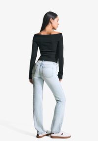 Black ribbed off-the-shoulder top with long sleeves, paired with light blue straight-leg jeans and white sneakers with brown soles.