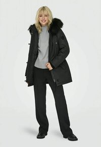 Black insulated parka with fur-trimmed hood, front zipper, and snap buttons. Worn over a gray sweater and black pants. Smooth texture.
