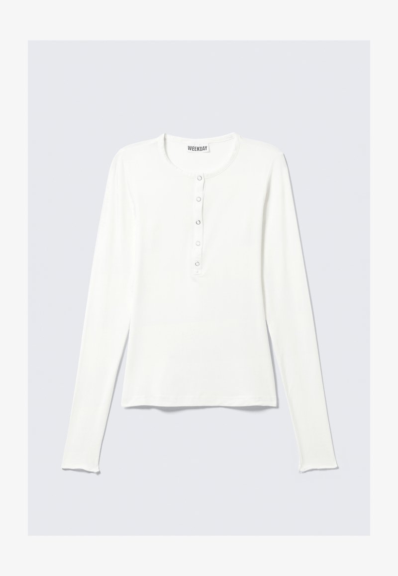 Camisa blanca de manga larga con escote redondo, tapeta de botones en el frente y una textura suave. Diseño sencillo y corte relajado.