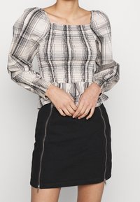 Ljusbeige topp med svart rutmönster, puffärmar och smockad midja, i kombination med en svart kjol med dragkedja fram.