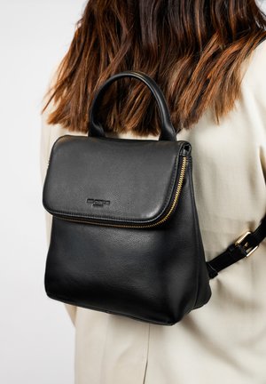 Sac à dos en cuir noir avec fermeture éclair, surface texturée, forme arrondie, poignée supérieure et bandoulière ajustable. Design minimaliste.