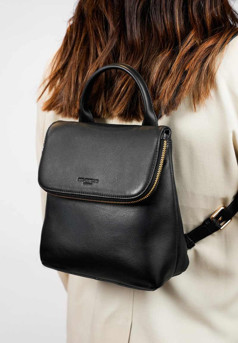 Zwarte leren rugzak met een ritssluiting, gestructureerd oppervlak, afgeronde vorm, bovenhandvat en verstelbare schouderband. Kenmerken van een minimalistisch ontwerp.