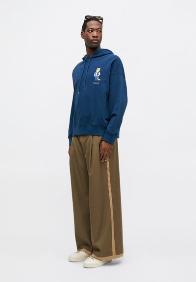 Sudadera azul marino con gráfico frontal, capucha con cordón y puños acanalados. Combinada con pantalones de pierna ancha color arena que cuentan con una franja lateral.