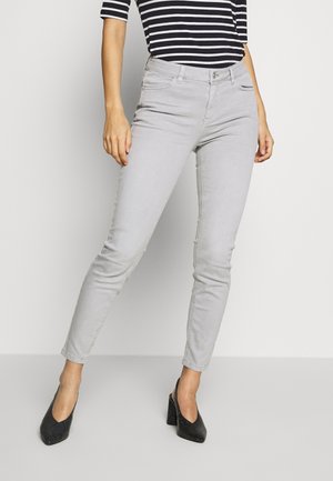 Dopasowane jasnoszare dżinsy noszone z czarno-białym paskowanym topem i czarnymi butami na wysokim obcasie z blokowym obcasem.