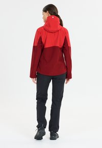 Red and dark red waterproof jacket with a hood, long sleeves, and adjustable cuffs, paired with black pants and rugged black footwear.