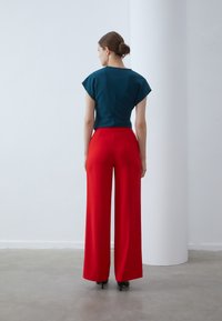 Teal top with cap sleeves paired with high-waisted, wide-leg red pants. Both garments feature smooth textures and a tailored fit.