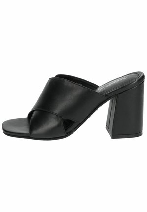 Mules negros de tacón con un diseño de cuero suave. Presentan un diseño de tiras cruzadas y un tacón cuadrado y grueso. Estilo de punta abierta.