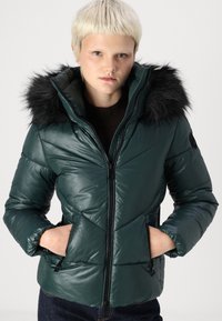 Dark green puffer jacket with a faux fur-trimmed hood, zip closure, and diagonal stitching. Features side pockets and a slim fit design.