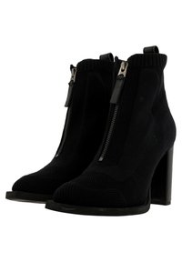 Une paire de bottines noires à talons hauts chunky, avec des zips à l'avant, des bords supérieurs côtelés, fabriquées en tissu tricoté.