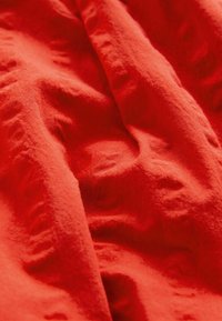 Czerwony materiał o miękkiej, teksturowanej powierzchni; układany z widocznymi zagięciami i fałdami. Jednolity kolor bez wzorów czy wyraźnych detali.