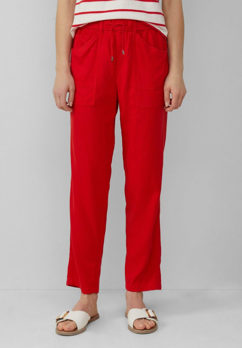Czerwone spodnie z troczkami, z dwoma przednimi kieszeniami, luźny krój, lekką tkaninę, w połączeniu z białymi sandałami z ozdobną klamrą.