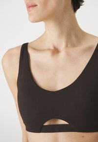 Melnās krūšturis ar lapu izgriezumu un horizontālu izgriezumu priekšpusē. Izgatavots no gluda materiāla, ar platām plecu siksnām.