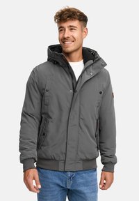Chaqueta acolchada gris con capucha, que presenta un cierre frontal con cremallera, botones a presión y bolsillos laterales. Tejido texturizado con puños y dobladillo de canalé.