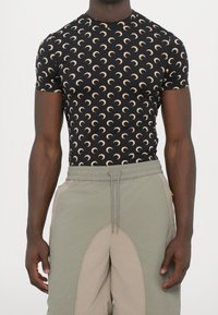 Svart kortärmad skjorta med ett upprepande mönster av halvmånar i beige. Lager av grå och beige sweatpants med dragsko i midjan.