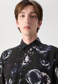 Schwarze Hemdbluse mit großen abstrakten Rosenmustern in Blau- und Weißtönen, klassischem Kragen und glatter Textur.