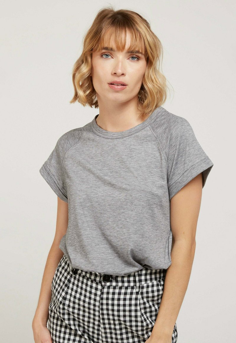 Chemise grise à manches courtes avec une coupe décontractée et un col rond, fabriquée en tissu doux, associée à un pantalon à carreaux noir et blanc.